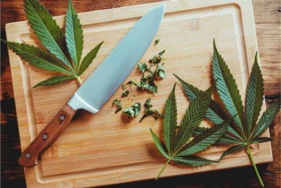 Foglie di cannabis fresche su tagliere di legno con coltello da cucina – preparazione per ricette alimentari